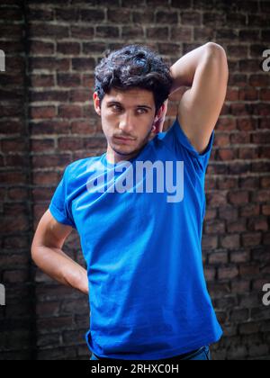 Drei Viertel Schuss von einem hübschen jungen Mann im urbanen Setting, der ein blaues Poloshirt vor einer Ziegelmauer trägt Stockfoto