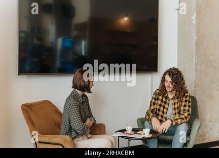 Vorderansicht eines langhaarigen Mannes und einer kurzhaarigen Frau, die während einer Pause von der Arbeit diskutieren Stockfoto