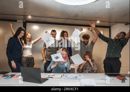 Geschäftsleute mit unterschiedlichen Altersgruppen, die sich gegenseitig umarmen und gemeinsamen Geschäftserfolg feiern. Geschäftsleute feiern erfolgreich spät in der Nacht Stockfoto