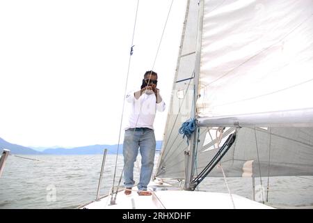 Ein Erwachsener Latino fährt ein Segelboot auf dem See mit Segeln, die als körperliche Aktivität, Sport und Hobby entwickelt wurden, um sich am Wochenende zu entspannen Stockfoto