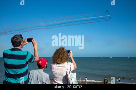 Eastbourne, Großbritannien. August 2023. Eine Familie beobachtet vom Eastbourne Beach aus, wie das weltberühmte RAF-Anzeigeteam The Red Arrows auf der jährlichen Eastbourne Airbourne, einer internationalen Flugschau, an der Küste vorbeifliegt. Die Show findet vier Tage lang statt, mit Flugvorführungen entlang der Küste. Stockfoto