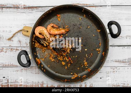 Blick von oben auf die Pfanne mit spanischen Paella-Resten von Reis mit Muschel und Garnelen auf Holztisch in der Küche Stockfoto