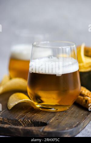 Leckere Stücke knuspriger Kartoffelchips in einer Schüssel mit Brotstöcken und Gläsern Bier auf Holzbrett, die bei Tageslicht über den Tisch gestellt werden Stockfoto