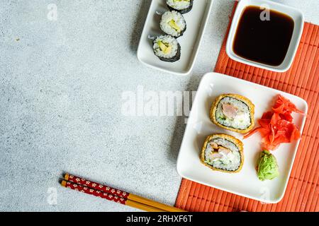 Von oben verschiedene Sushi-Brötchen auf Tellern mit Stäbchen und Sojasauce auf weißem Hintergrund Stockfoto