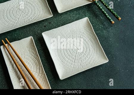 Von oben aus dem Set von weißen Keramikplatten auf schwarzem Betontisch mit Stäbchen im asiatischen Restaurant Stockfoto