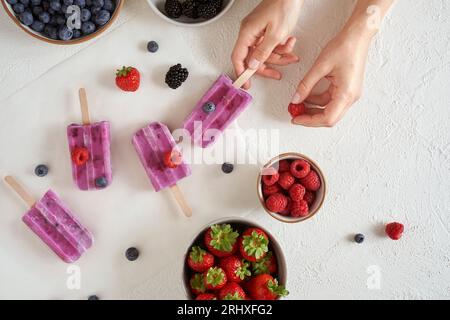 Top-Ansicht der anonymen Frau mit hausgemachtem veganem Bio-Protein-Eis auf weißer Oberfläche in der Nähe von Schüsseln mit verschiedenen frischen Früchten Stockfoto