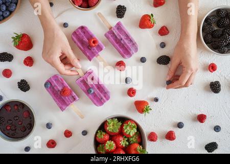 Top-Ansicht der anonymen Frau mit hausgemachtem veganem Bio-Protein-Eis auf weißer Oberfläche in der Nähe von Schüsseln mit verschiedenen frischen Früchten Stockfoto