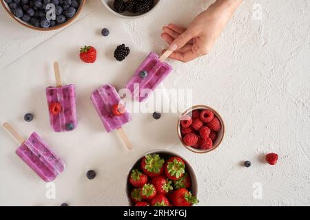Top-Ansicht der anonymen Frau mit hausgemachtem veganem Bio-Protein-Eis auf weißer Oberfläche in der Nähe von Schüsseln mit verschiedenen frischen Früchten Stockfoto