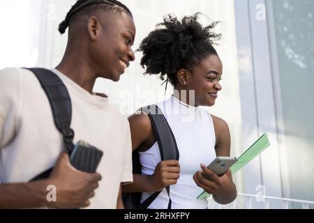 Porträt eines positiven jungen afroamerikanischen Schülerpaares im Teenageralter in lässiger Kleidung mit Afro-Frisur und Rucksäcken, die lächeln und wegschauen Stockfoto