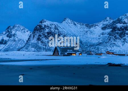 Malerischer Blick auf verschneite Berge und Häuser am Ufer gegen Himmel im Winter Lofoten Inseln Stockfoto