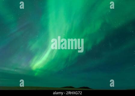 Spektakuläre Landschaft mit grünen Nordlichtern, die den dunklen Himmel über grünen Wiesen und Bergen erleuchten Stockfoto