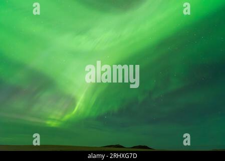 Spektakuläre Landschaft mit grünen Nordlichtern, die den dunklen Himmel über grünen Wiesen und Bergen erleuchten Stockfoto