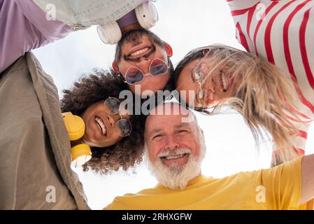 Von unten sind fröhliche, vielfältige Freunde, die lachen und im Kreis stehen, während sie sich gegenseitig umarmen und miteinander Spaß haben Stockfoto