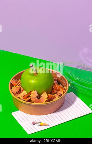 Von oben gesunder Apfel umgeben von Bleistiftspänen in der Lunchbox in der Nähe von Papier auf grünem Tisch Stockfoto