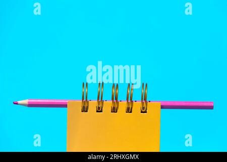 Gelbes Notizbuch mit Hardcover und pinkfarbenem Bleistift auf blauem Hintergrund bei Tageslicht Stockfoto