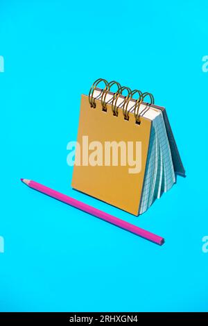 Draufsicht auf Schreibwaren Spiralring gebundene weiße Papiere Notizbuch mit Hardcover und schärfem violetten Bleistift zusammen gegen blu platziert Stockfoto