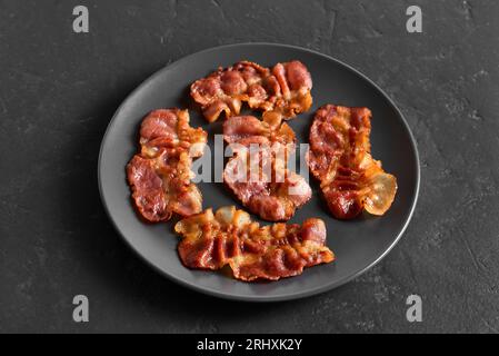Gerösteter Speck auf Teller auf schwarzem Steinhintergrund. Nahansicht Stockfoto