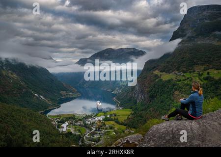Tourist in Norwegen - Frau bewundert Blick von landschaftlich reizvollen Punkt auf einem Hügel, Kreuzfahrt Boot entlang Geiranger und Geirangerfjorden. Stockfoto