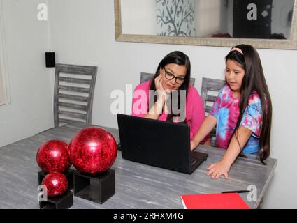 Latina Mutter und Tochter, die aufgrund der COVID-19-Pandemie im Esszimmer mit einem Laptop und Notebook zur Quarantäne zu Hause Schule machen Stockfoto