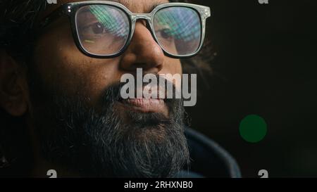 Nachdenklicher, ernsthafter indischer Geschäftsmann in Brillenfassung, der sich in Gedanken und Gedanken verloren hat. Nahaufnahme fokussierter nachdenklicher bärtiger arabischer Mann mit Lichtern Stockfoto