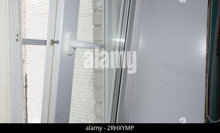 Das doppelverglaste Fenster ist weiß mit Rollläden. Das Fenster ist nicht richtig geöffnet. Fensterreparatur, Bruch Stockfoto