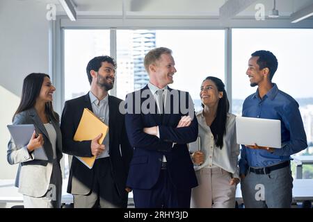 Fünf junge, glückliche Geschäftsleute aus dem professionellen Team, die im Büro stehen und lachen. Stockfoto