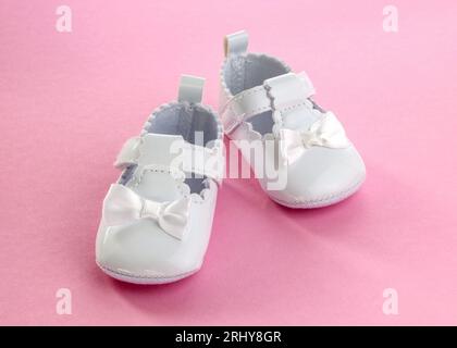 Weiße Hausschuhe mit Schleife für ein kleines Mädchen. Paar Babyschuhe. Babyschuhe auf rosafarbenem Hintergrund. Jeansschuhe für Mädchen. Stockfoto