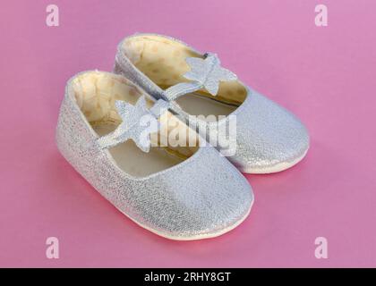 Paar Babyschuhe. Babyschuhe auf rosafarbenem Hintergrund. Jeansschuhe für Mädchen. Silberne Hausschuhe mit einem Stern für ein kleines Mädchen. Stockfoto