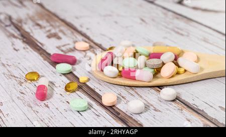 Vitaminkapseln in einem Holzlöffel auf farbigem Hintergrund. Pillen als gesunde Mahlzeit serviert. Drogen, Apotheke, Medizin oder medizinisches Gesundheitskonzept. Stockfoto