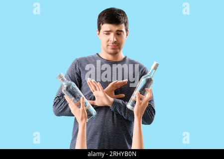 Junger Mann, der Wodkaflaschen auf blauem Hintergrund ablehnt Stockfoto