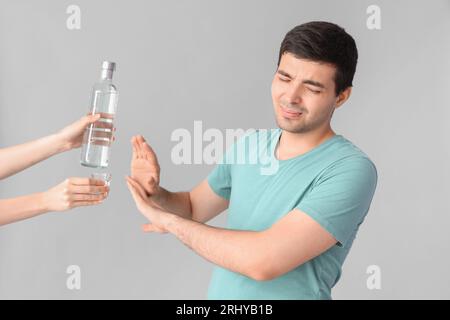 Junger Mann, der Wodka auf hellem Hintergrund ablehnt Stockfoto