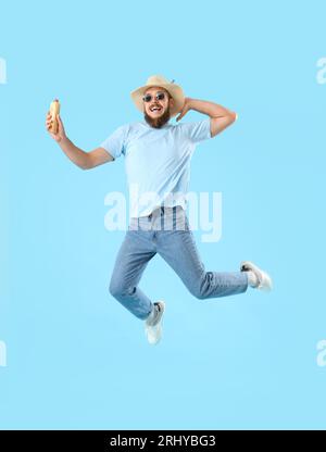 Schöner junger Mann, der mit leckerem Hot Dog auf blauem Hintergrund springt Stockfoto