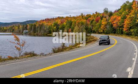 Jeep on Scenic Highway - Ein Jeep-SUV, der entlang des Beaver Pond auf der gewundenen Route 17, Teil des Rangeley Lake Scenic Byway, an einem farbenfrohen Herbstmorgen fährt. Stockfoto