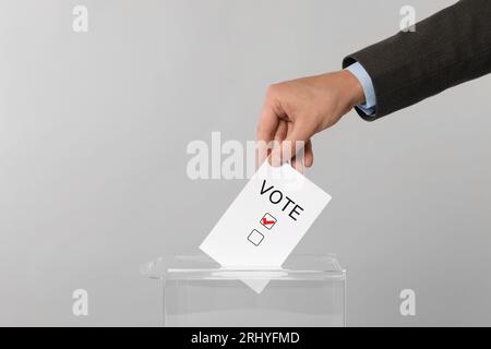 Mann, der Papier mit Wortwahl und Haken in die Wahlurnen auf hellgrauem Hintergrund legt Stockfoto