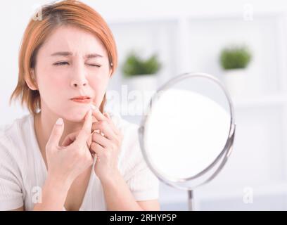 Junge Frau, die Pickel zusammendrückt, um sie aus dem Gesicht zu entfernen. Stockfoto