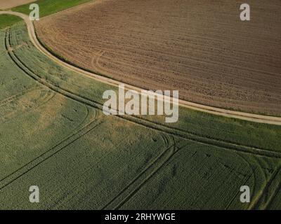 Luftaufnahme eines Ackerlandes mit gepflügtem Schotterfeld, einer Schotterstraße und einem grünen Feld im Frühjahr Stockfoto