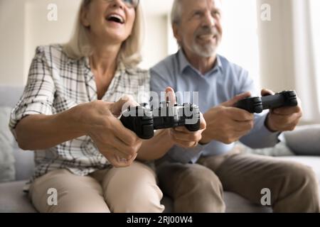 Fröhlicher älterer Mann und Frau, die auf Gamepads Knöpfe drücken Stockfoto