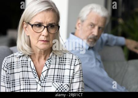 Gestresste, reife Frau, die sich ängstlich fühlte, nachdem ein verärgerter, älterer Ehemann dahinter war Stockfoto