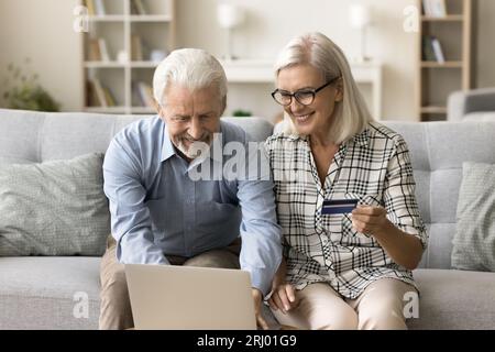 Ein fröhliches altes pensioniertes Paar, das Kreditkarte und Laptop benutzt Stockfoto