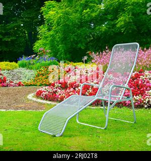 Liegestuhl im Park neben dem Blumenbeet Stockfoto