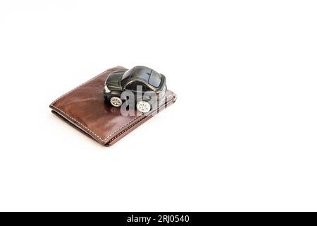 Spielzeugauto auf Geldbörse isolierter weißer Hintergrund. Kfz-Versicherung oder Spesenkonzept. Stockfoto