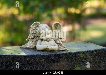 Kleiner Engel auf dem Grabstein mit einem Herz in den Armen Stockfoto