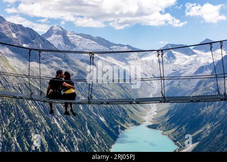 Zillertaler Alpen, Österreich. August 2023. Eine Frau und ein Mann küssen sich auf einer Hängebrücke auf einem Wanderweg in den Zillertaler Alpen - mit Blick auf den Schlegeis-Stausee und die umliegenden Alpengipfel. Quelle: Frank Hammerschmidt/dpa/Alamy Live News Stockfoto