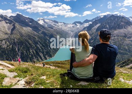 Österreich. August 2023. Eine Frau und ein Mann sitzen auf einem Wanderweg in den Zillertaler Alpen und blicken hinunter auf den Schlegeis-Stausee. Der Stausee ist einer von fünf Stauseen im Zillertal und umfasst eine Fläche von etwa 220 Hektar. Es ist der Ausgangspunkt für eine Vielzahl beliebter Wanderungen. Quelle: Frank Hammerschmidt/dpa/Alamy Live News Stockfoto