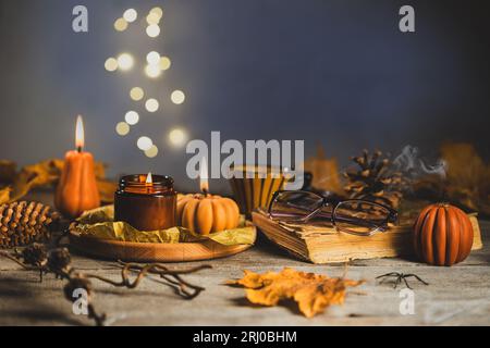 Halloween Stillleben auf dem Holztisch. Kürbiskerzen mit trockenen Kegeln und Blättern, altem Buch und Gläsern. Bokeh-Lichter im Hintergrund Stockfoto