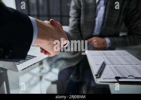 Agent und Kunde schütteln sich die Hand, nachdem sie das Dokument unterzeichnet und einen Geschäftsabschluss für die Übertragung des Eigentumsrechts abgeschlossen haben. Stockfoto