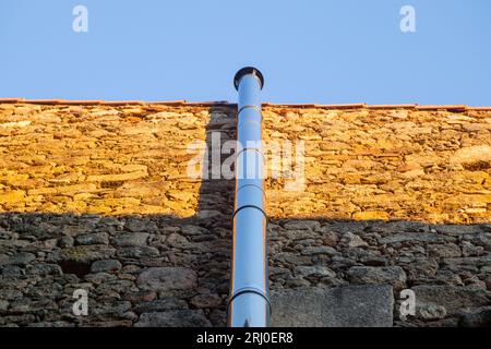 Verchromter Metallschornstein an einer Trockensteinwand befestigt. Bei Sonnenuntergang Stockfoto