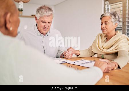 Ältere Freunde, Gebet und Hände in der Wohnung, Bibelstudium und Hoffnung im geistlichen Glauben. Senioren, Gruppe und Religion am Tisch Stockfoto