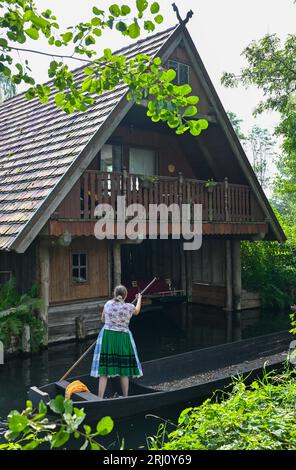 Burg, Deutschland. August 2023. Eine Frau in sorbisch-wenisch-traditioneller Tracht reist auf einem Holzkahn auf einem Fluss (Wasserstraße) im Spreewald. Quelle: Patrick Pleul/dpa/Alamy Live News Stockfoto