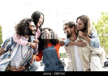 Eine multirassische Gruppe von Freunden, die Huckepack reiten und sich gegenseitig sehen. Verschiedene junge Frauen und Männer, die sich umarmen, lachen und sorglos Stockfoto